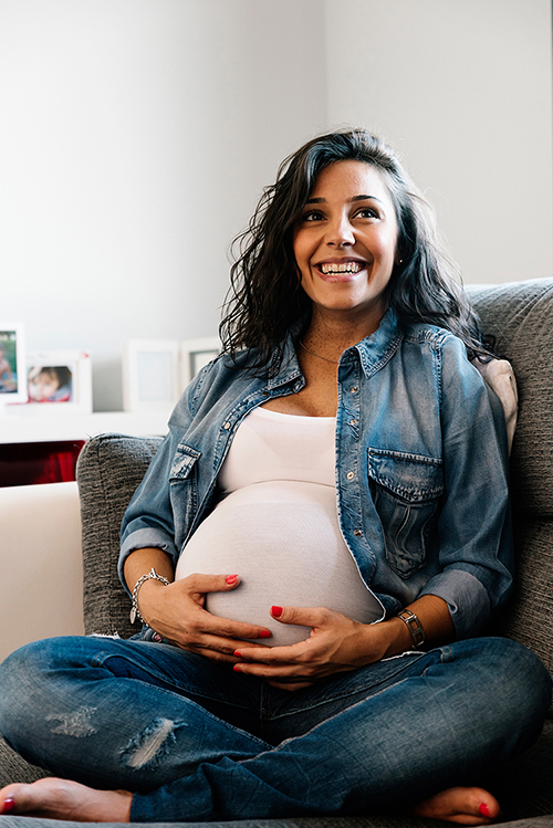 Happy pregnant woman smiling, holding her belly, looking up
