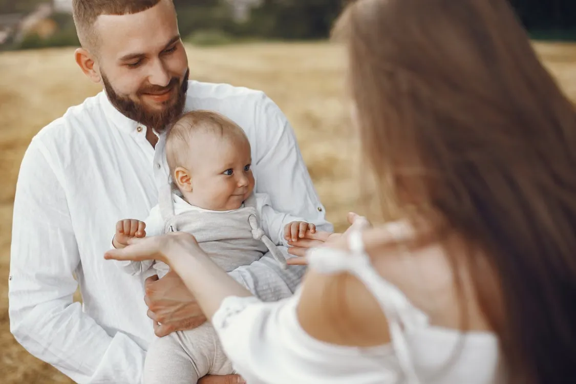 Parents reaching for their smiling baby together.